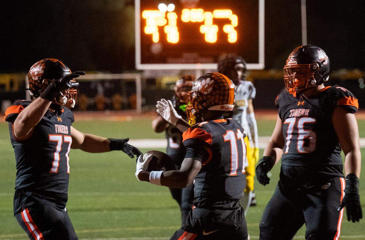 Roseville Tigers wide receiver Kenny McClure (11) celebrates a touchdown reception with guard Trevor Kirby (77) and tackle Caleb Barba (76) against the Hughson Huskies in the second half of a CIF Sac-Joaquin Section Division IV semifinal in Roseville on Friday, Nov. 21, 2025. 