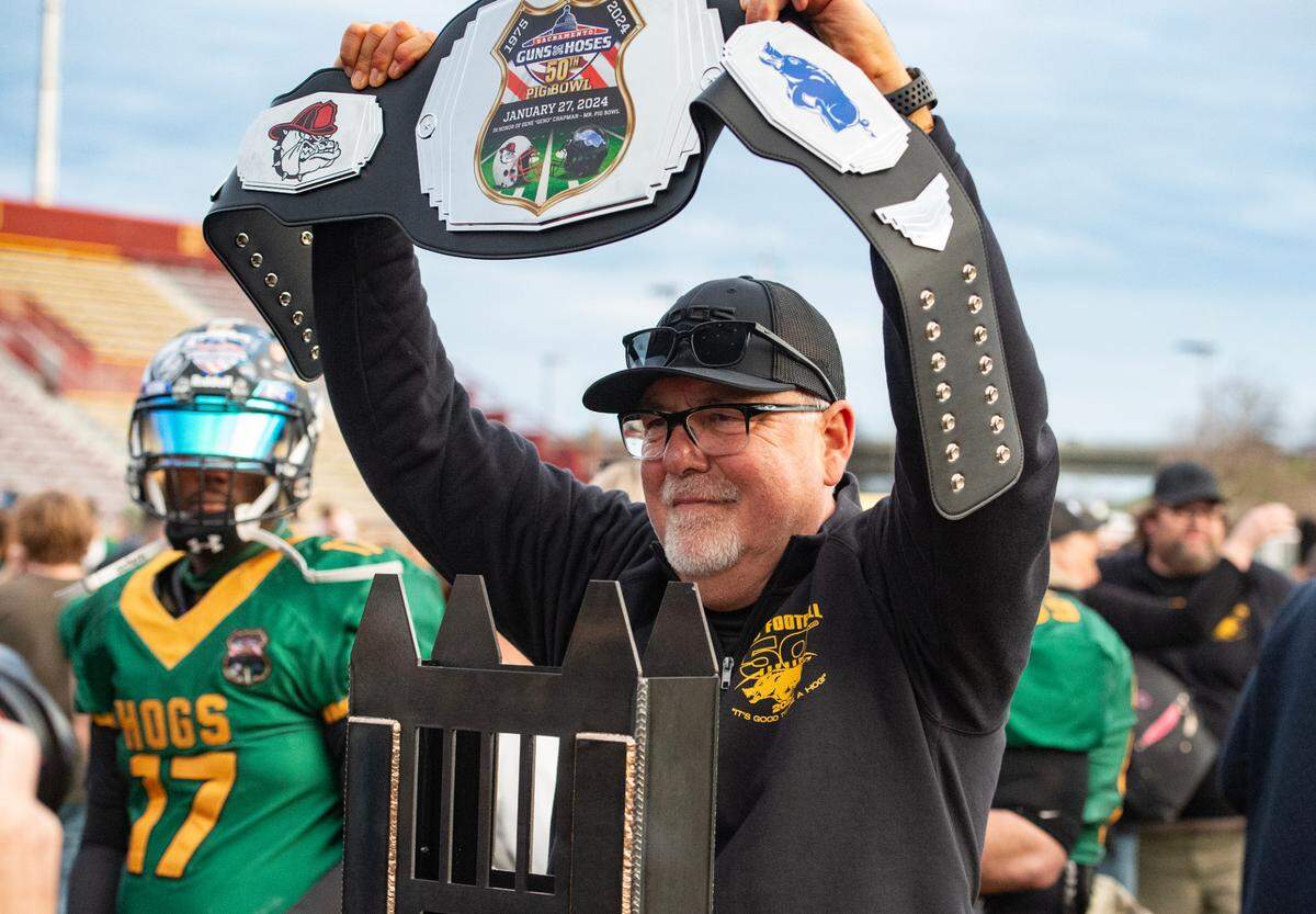 Law Hogs coach Mike Morris holds up a victory belt behind the Pig Bowl Guns vs Hoses trophy after the 50th anniversary game at Hughes Stadium on Saturday. The former Rio Linda High School coach finished his Pig Bowl career with a 9-3 record.
