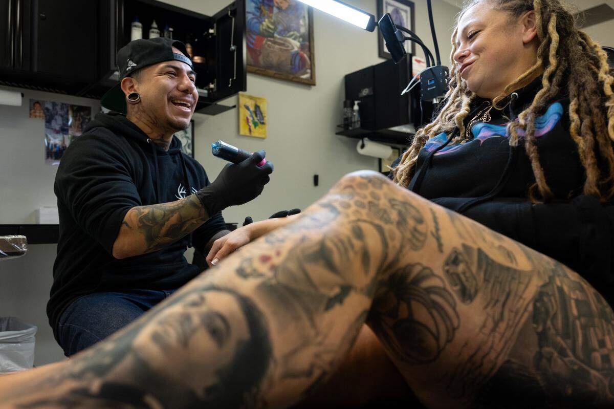 Tattoo shop owner Edgar Avila touches up a tattoo for customer Sarah Duplantier at Elk Grove Tattoo on Friday, Dec. 8, 2023. Avila created the tattoos of Duplantier’s family on her leg.