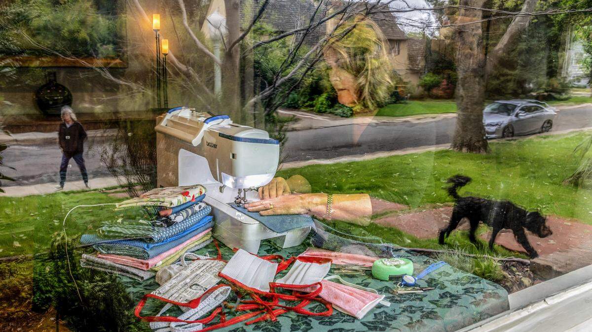 Brenda Fotos is seen through her front window in her living room sewing masks to donate to area hospitals as a Curtis Park neighbor walks past with her dog, Thursday, April 9, 2020. Fotos is one of many members of the Sacramento chapter of the American Sewing Guild making masks to help keep medical workers safe during the coronavirus pandemic.