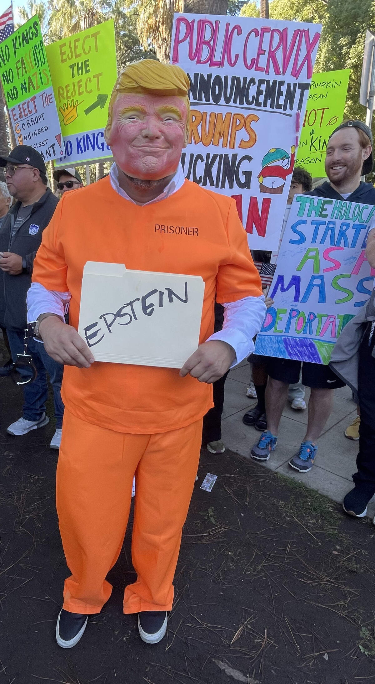 Brandon Baker dresses up as Donald Trump in a jumpsuit while holding a Manila envelope with the word “Epstein” at the “No Kings” protest in Sacramento Oct. 18, 2025