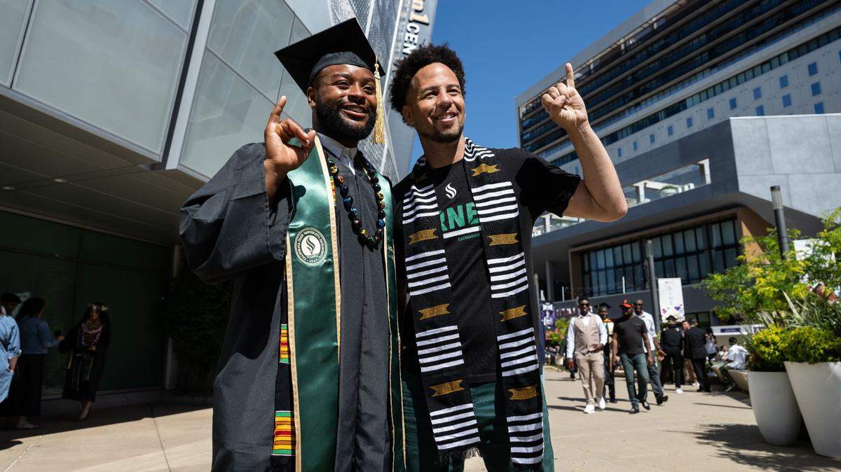 Sacramento State graduate Paul Lawrence Dunbar Banks makes the “stingers up” hand gesture with university President Luke Wood for a photo after the 2024 commencement ceremony at Golden 1 Center.