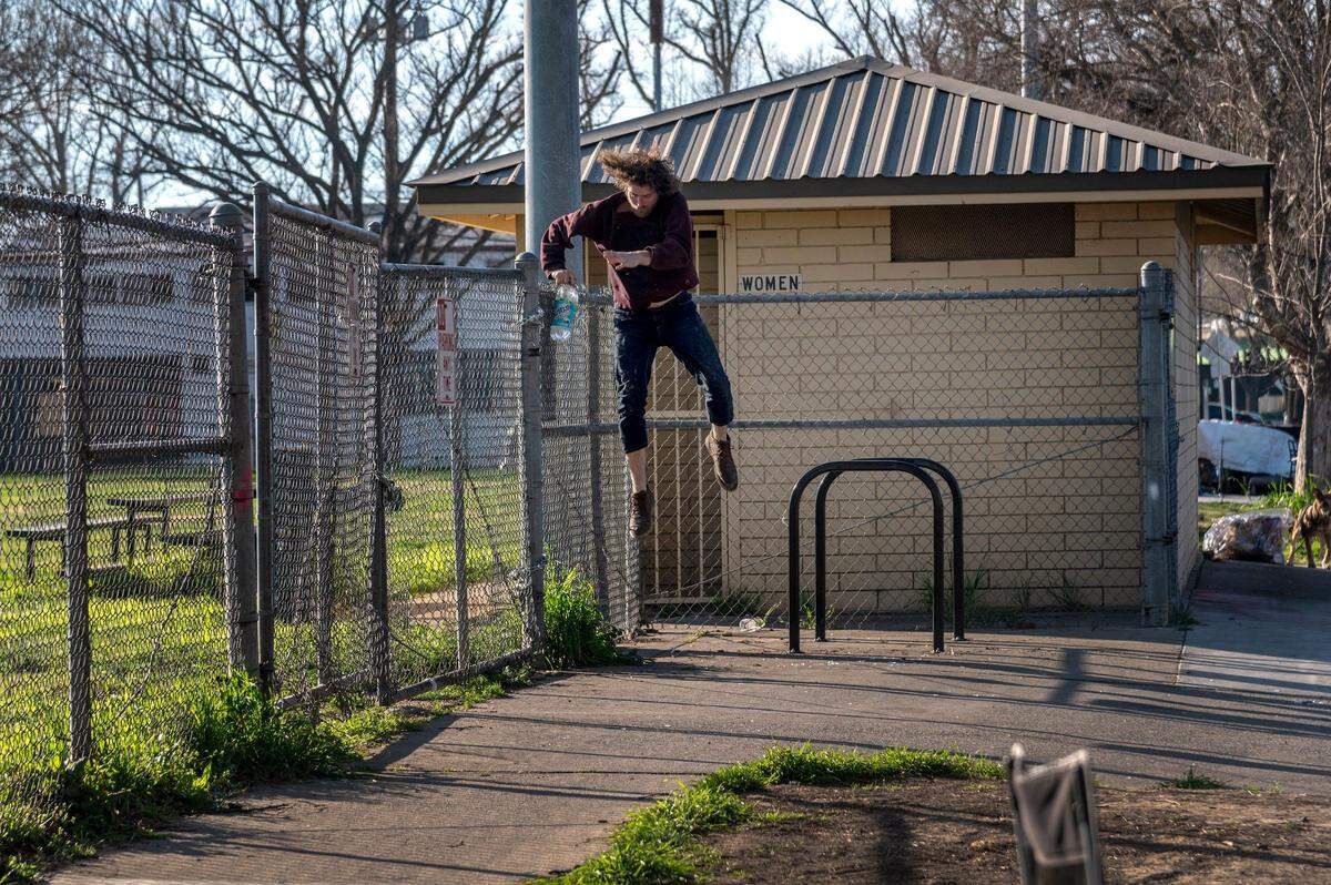 Justin, who wanted his last name withheld, jumps back over a locked fence after filling a bottle of water at a city park in Sacramento on Wednesday. He lived along W Street in a tent along several homeless campers who said they wished the city park restrooms and water fountain were accessible.