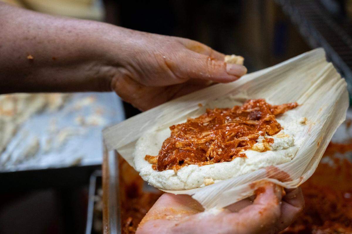 A pinch of shredded chicken in a tomato-chili sauce rests on masa dough in a corn husk before the tamal is sealed at Yolanda’s Tamales Factory in Sacramento in 2022. 