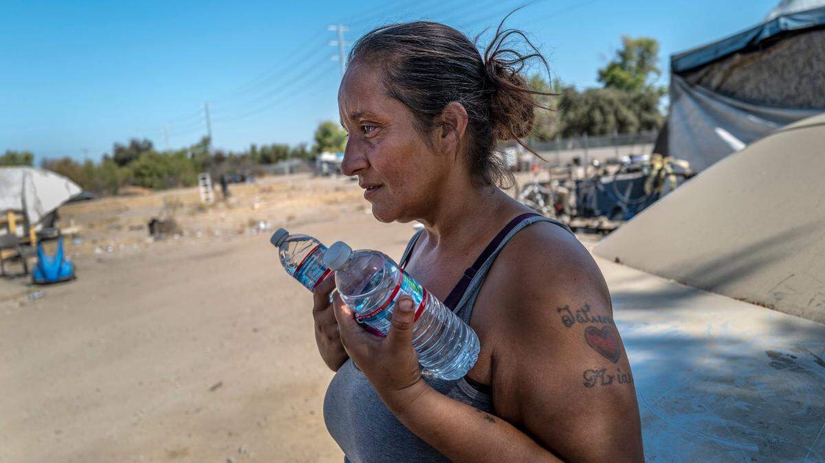Celina Gallegos, 42, holds water passed out by the city of Sacramento’s Department of Community Response at the “Snake Pit” homeless encampment in Sacramento on Thursday, Sept. 8, 2022. On her shoulder are two of the six tattoos she has with her childrens names.