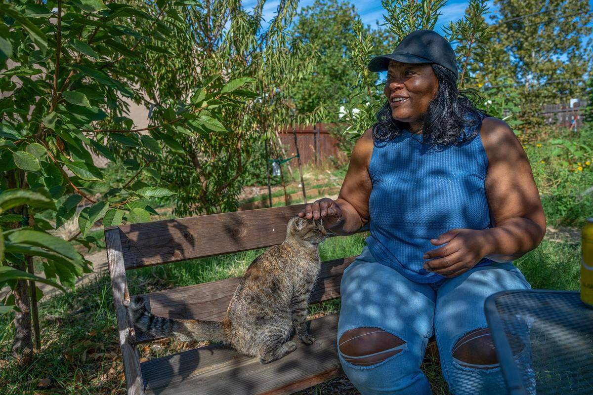 Robin Moore, 61, rests earlier this month with her cat Cookie in a community garden full of fruit trees, flowers and home grown vegetables next door to the Safe Harbor tiny home community she created. Once a weed-covered vacant lot, Moore leased the property and found volunteers to help her transform it into a community garden.