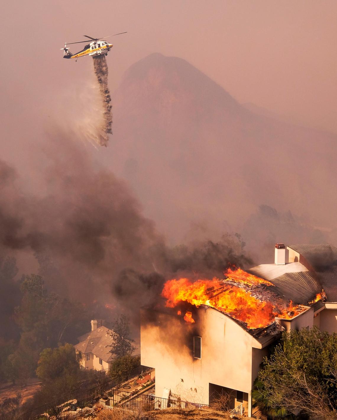 A helicopter drops water while a wildfire burns a home near Malibu Lake in Malibu, Calif., Friday, Nov. 9, 2018.  About two-thirds of the city of Malibu was ordered evacuated early Friday as a ferocious wildfire roared toward the beachside community that is home to about 13,000 residents, some of them Hollywood celebrities. (AP Photo/Ringo H.W. Chiu)