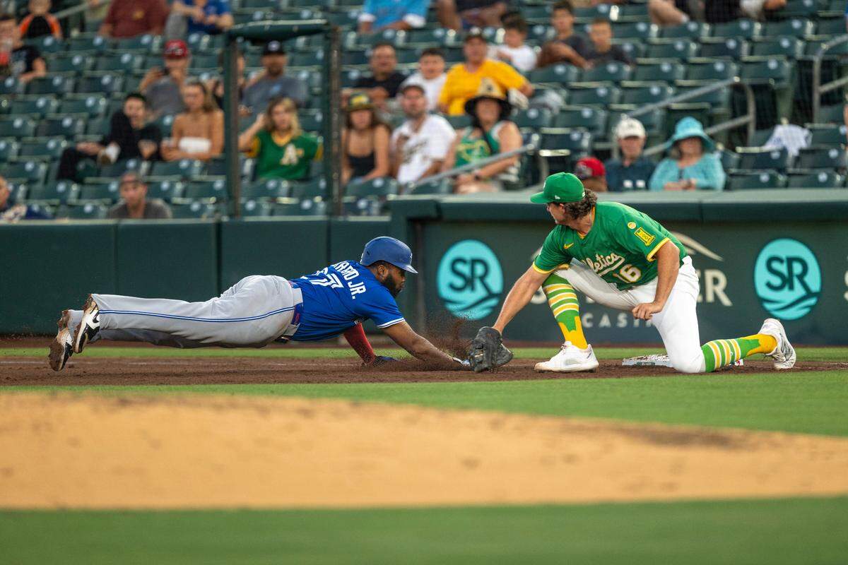 Toronto Blue Jays first baseman Vladimir Guerrero Jr. (27) dives back into first base as Athletics first baseman Nick Kurtz (16) attempts to apply a tag in the fifth inning of a game between the A’s and Toronto Blue Jays at Sutter Health Park in West Sacramento on Friday.