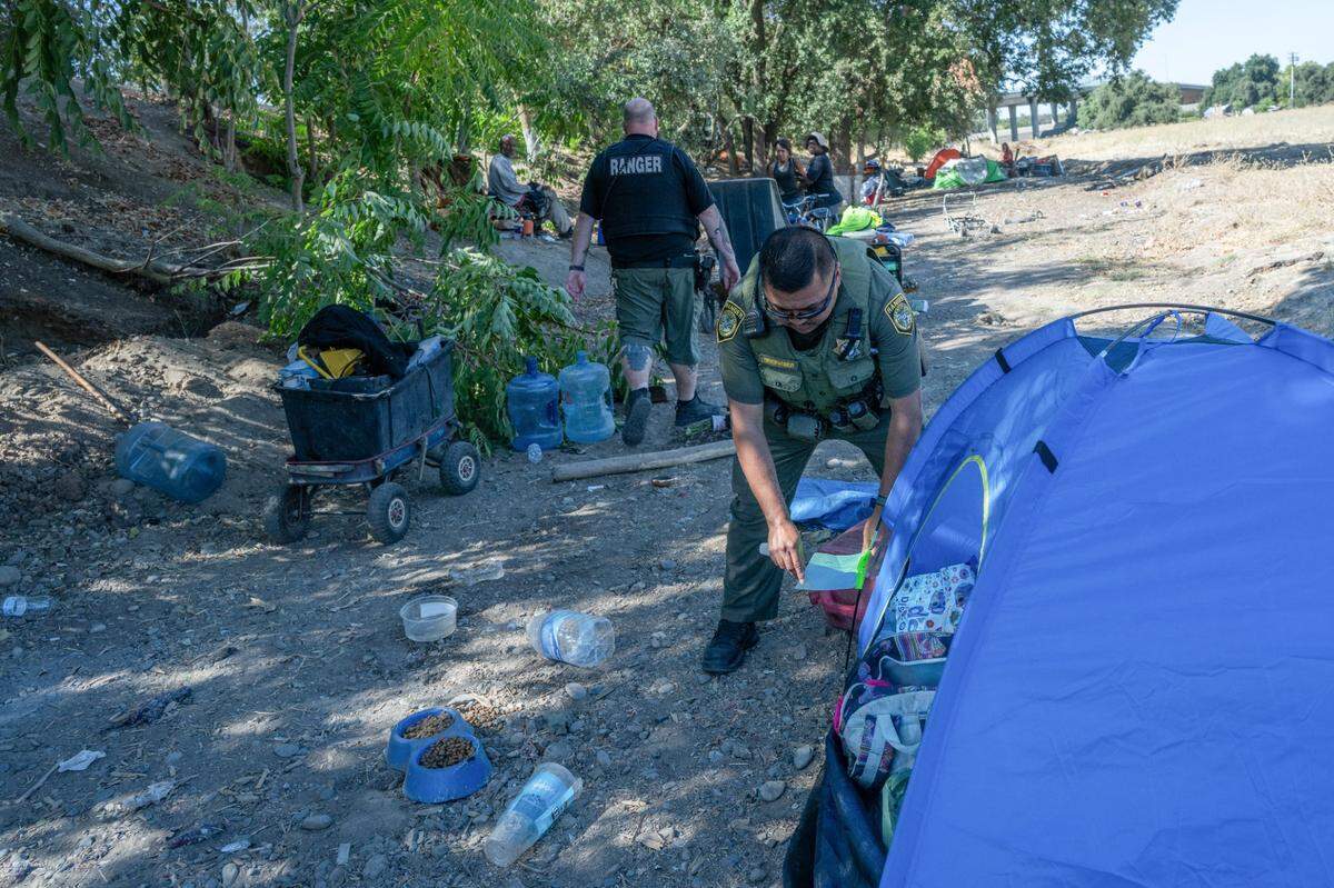 Sacramento park ranger Karl Tolentino-Stanley tags tents Wednesday with a notice to immediately vacate their campsite near the bike trail close to the Camp Resolution site. The campers, all displaced residents of the longtime homeless encampment, would not abandon their dogs for the shelter beds the city offered.
