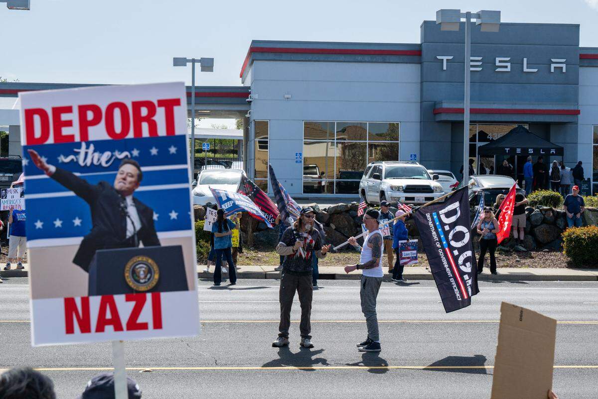 Anti-Tesla demonstrators wave signs across the street from the Tesla dealership in Rocklin as DOGE supporters stand in the street on Saturday, March 29, 2025.