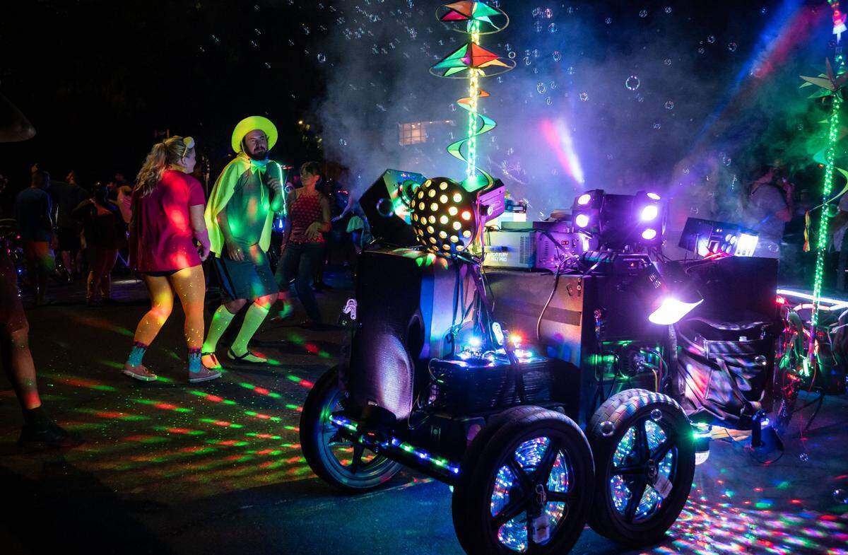 Kegan Craig wears a neon hat and costume as he dances with his girlfriend, Tara Singleton, left, to music coming from a mobile party bike during a stop at Crocker Park on Friday, Aug. 6, 2021, during Bike Party Sacramentos monthly riding event themed neon nights for August. The two met at a Bike Party Sacramento event three years ago. He kept trying to find me, like on the ride, she said, adding that Craig liked the jacket she wore during the 1970s-themed event bike ride that month. Id always bike up to the front, and then stop and wait for her, Craig added.