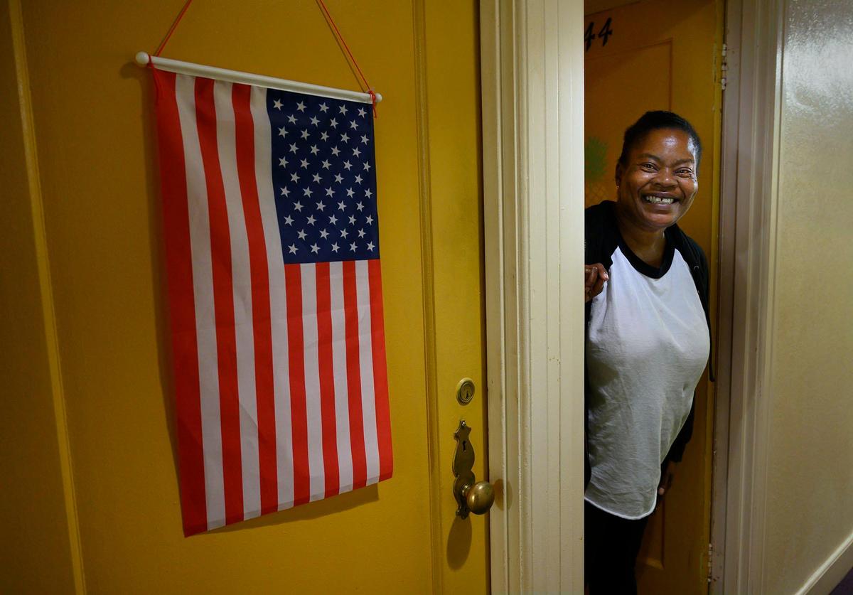 Resident Dionne Small, 50, peers out from her room where her neighbor displays a flag at the Capitol Park Shelter on Friday, November 15, 2019 in Downtown Sacramento. Small was homeless for seven years and slept outside the Sacramento courthouse. Volunteers of America’s Capitol Park Shelter is asking Book of Dreams readers for basic winter items for the homeless like, thermal socks, gloves, hats and rain coats.