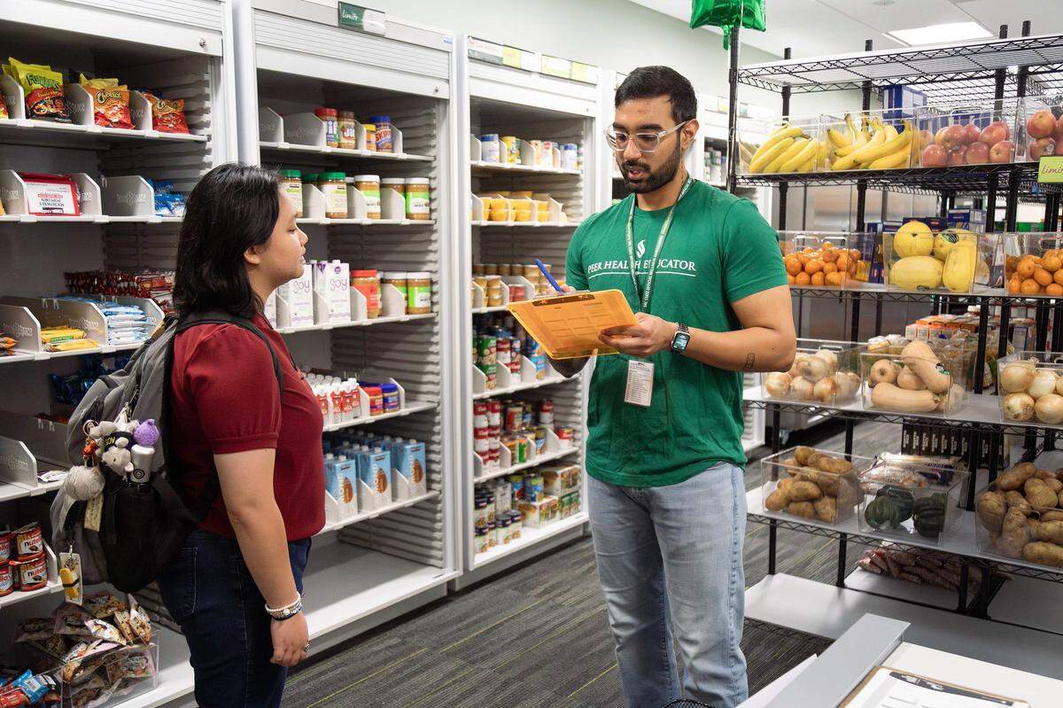 Student assistants Faith Ballesteros, left, and Naman Gusain rehearse the protocol for assisting shoppers at Sacramento State’s new basic needs center, each taking turns playing the roles of a client and a personal shopper.