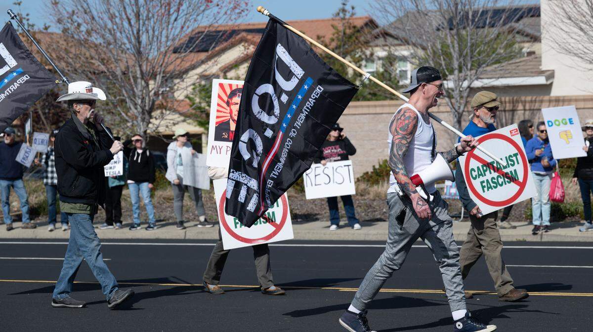 A MAGA counter protester with a DOGE flag marches down the center of Granite Drive in Rocklin near anti-Tesla protesters across from the Tesla dealership on Saturday, March 29, 2025.