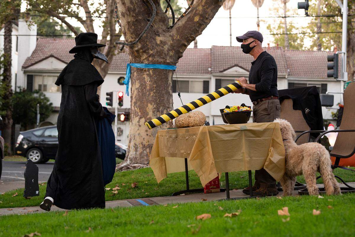 Trick-or-treater Ashton Coniglio, 13, left, who said he is dressed as a plague doctor, thanks resident Chris Conlin for candy, which he dispensed through a tube for social distancing, while celebrating Halloween amid the COVID-19 pandemic on Saturday, Oct. 31, 2020, in East Sacramento.