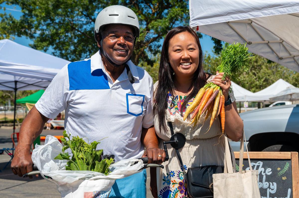 District 7 Sacramento City Councilmember Rick Jennings and District 8 Sacramento City Councilmember Mai Vang hold fresh produce purchased at the Meadoview Farmers’ Market in Sacramento on June 23.