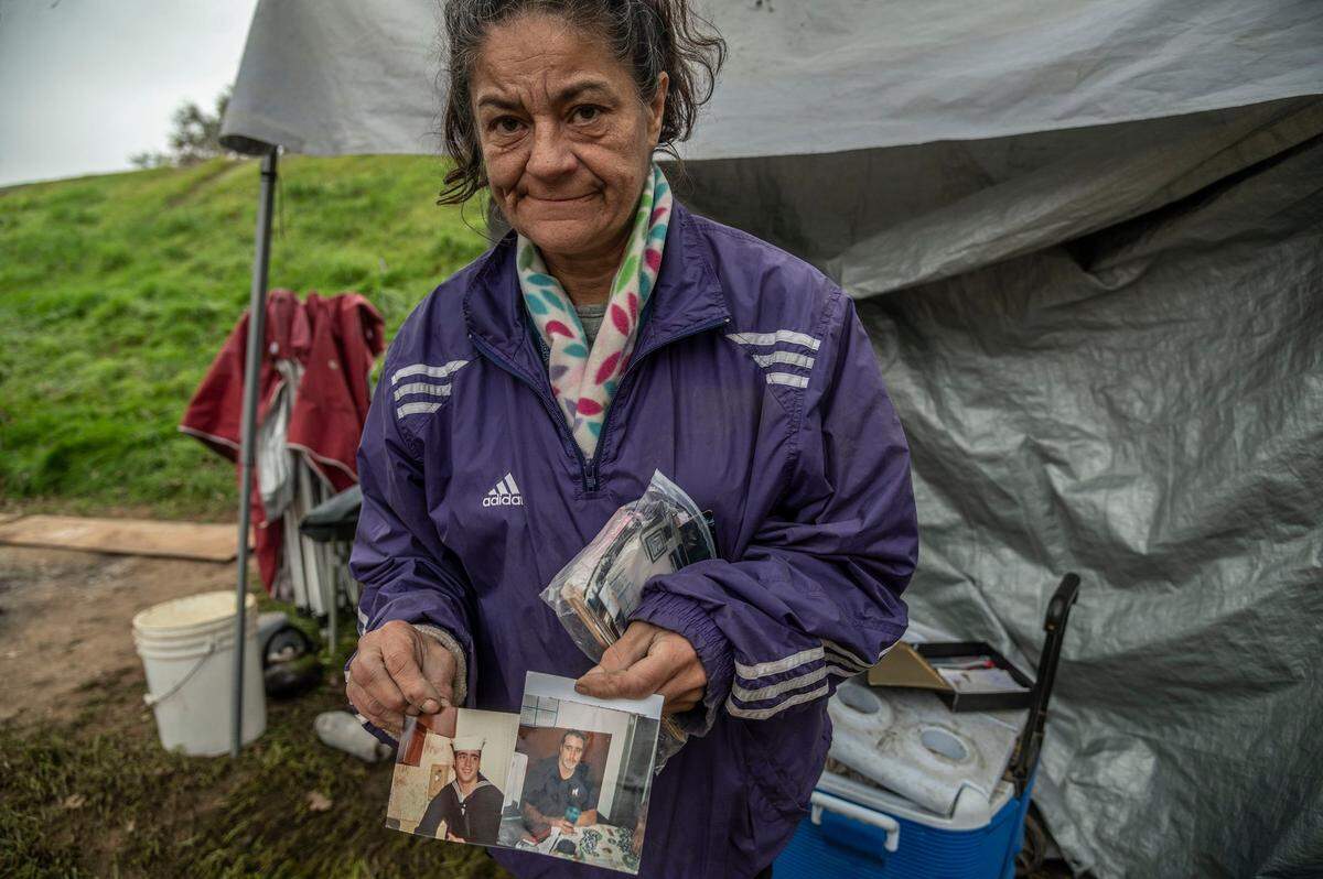 Outside her homeless tent encampment along Lathrop Way in Sacramento, Sandra Valadez holds photographs of Mike Trimble, her partner for twenty years, in December. She said he was found dead at the intersection of 19th and C streets on Nov. 22. The Coroner’s Office reported it as a homeless death.