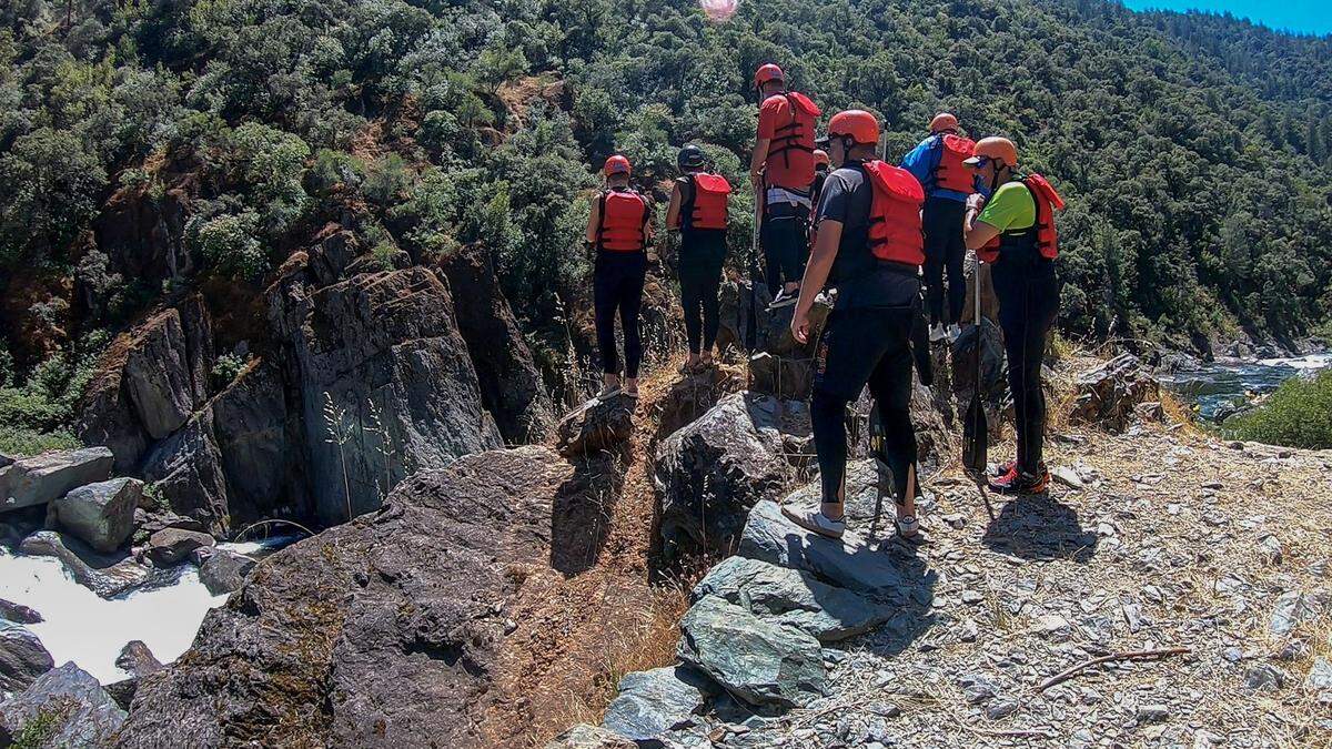 Participants of a rafting trip watch a guide with Sierra Whitewater maneuver raft over the Ruck-A-Chucky Falls on the Middle Fork of the American River on May 24, 2024. The falls are considered too dangerous for a loaded raft, so passengers disembark and hike around the obstacle.