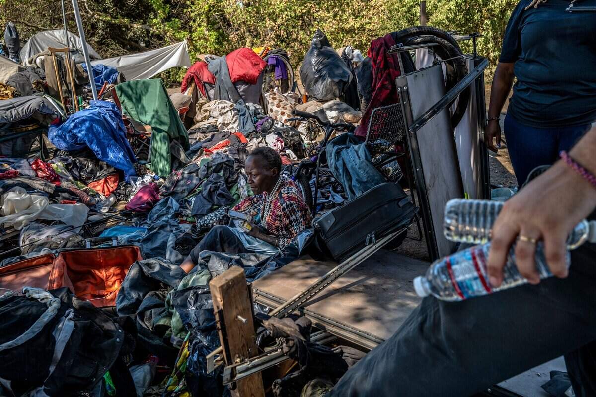 Latonya Haynes, 54, who said she is partially paralyzed, sits among her belongings in the “snake pit” homeless encampment in Sacramento on Thursday as Christopher Foxall, right, with the city of Sacramento Department of Community Response brings her water.