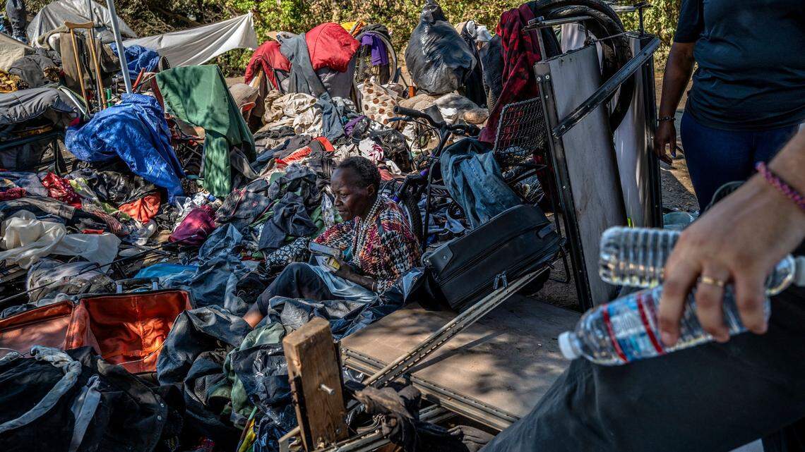 Latonya Haynes, 54, who said she is partially paralyzed, sits among her belongings in the “the snake pit” homeless encampment in Sacramento on Thursday, Sept. 8, 2022. as Christopher Foxall, right, with the city of Sacramento Department of Community Response brings her water. 