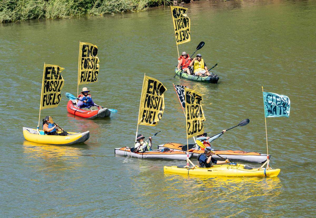 Climate activists kayak the Sacramento River with flags calling for an end to fossil fuels  during a protest on Sunday.