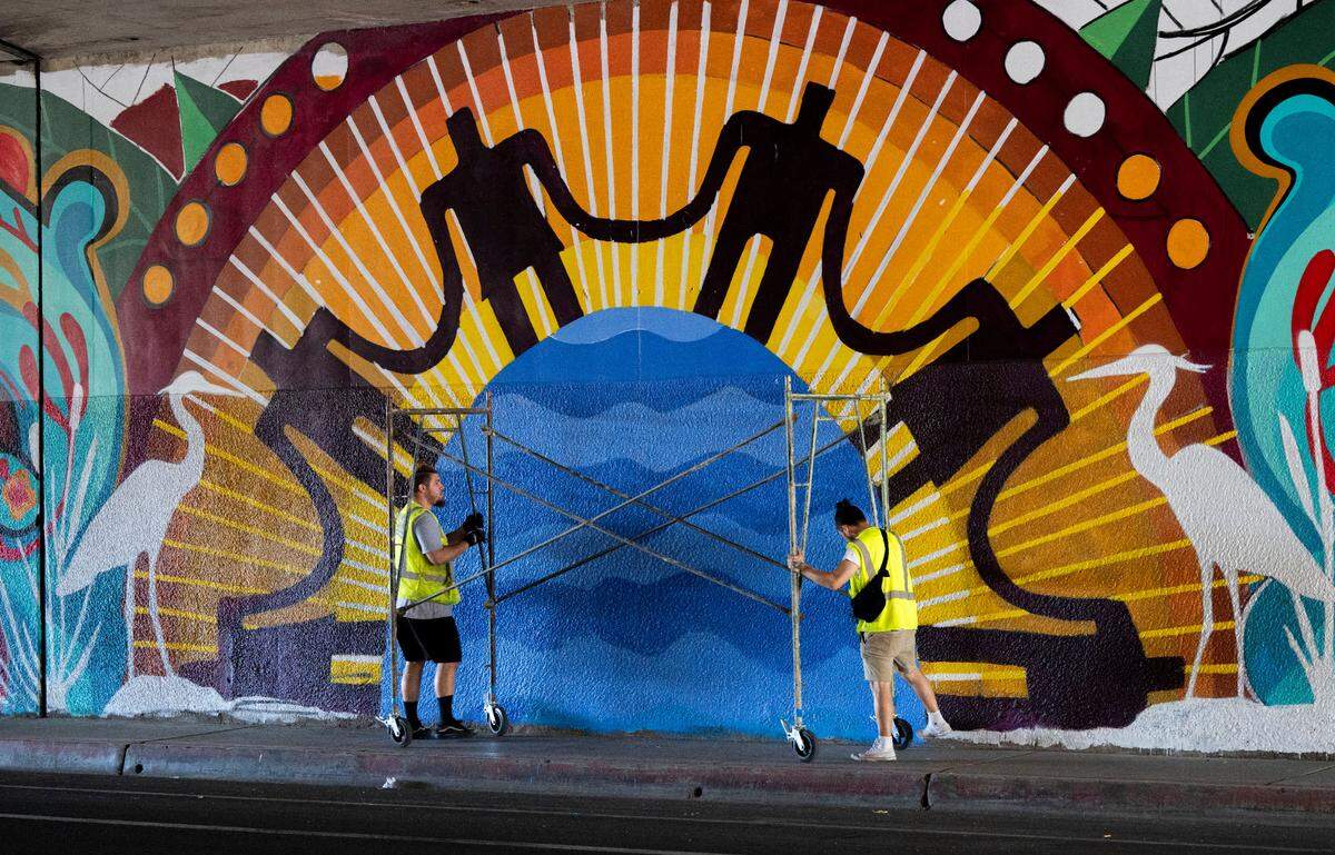 Young artists who work with José Lott push a rolling scaffold along the sidewalk in September to work on mural project on the Second Avenue Highway 99 underpass.