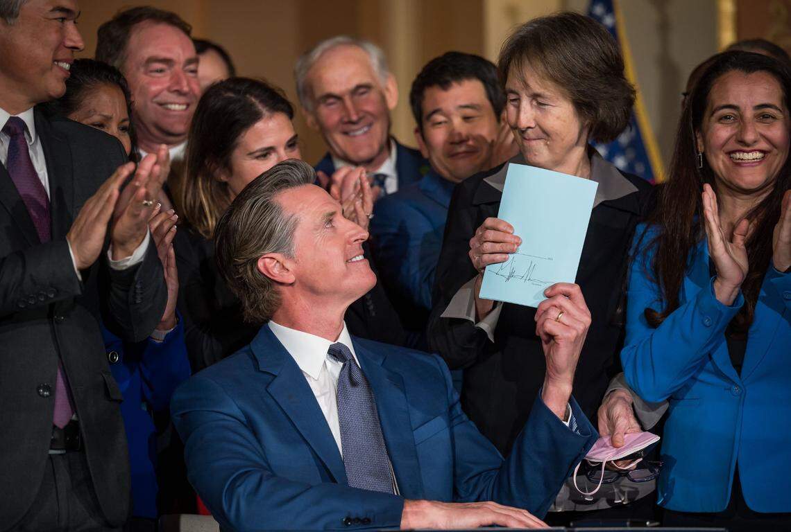 Gov. Gavin Newsom hands a signed bill aimed at addressing gas price gouging to author state Sen. Nancy Skinner, while surrounded by other legislators and state officials, after signing it in the Capitol rotunda on Tuesday, March 28, 2023. The California Assembly passed the bill Monday.