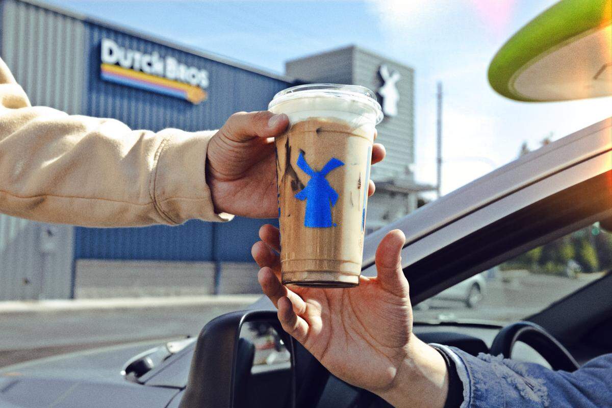 A Dutch Bros employee hands a customer an iced coffee drink.