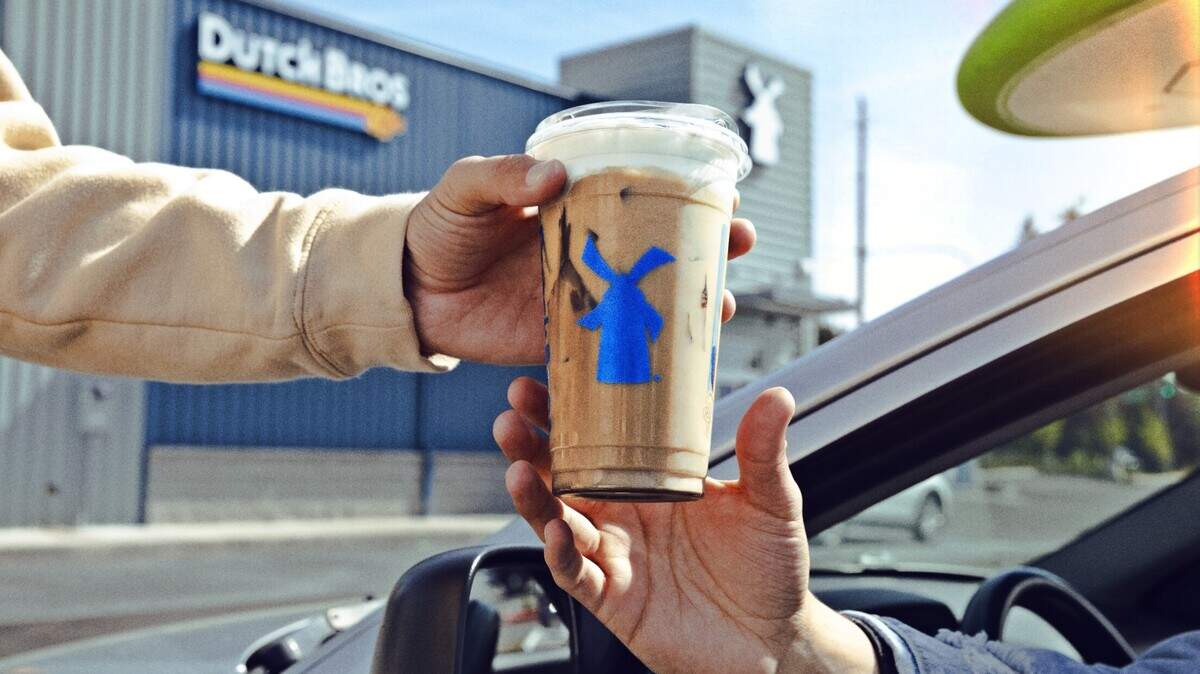 A Dutch Bros employee hands a customer an iced coffee drink.