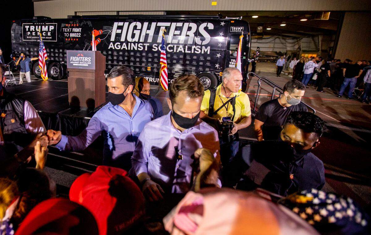 Donald Trump Jr.. left, wears a mask as he interacts with the crowd of Trump supporters at the “Fighters against Socialism” event at the Wings Over Miami Museum in Miami, Fla., on Sunday, Oct. 11, 2020. He is accompanied by adviser Taylor Budowich, wearing a gray mask at right.