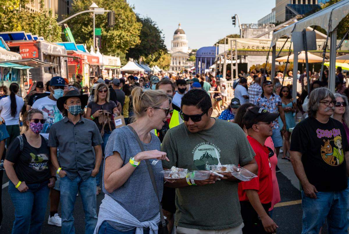 Emily Gardner, left, and Orlando Olivas, Sacramento residents who are engaged to be married, eat beignets and listen to live music at the&nbsp;Farm-to-Fork Festival on Saturday, Sept. 18, 2021, in downtown Sacramento. Olivas, who grew up in Sacramento and moved away 15 years ago, returned last January. “I’m surprised Sacramento has something like this going on,” he said. “Just to have the festival someplace downtown like this … it’s a good look for Sacramento.”