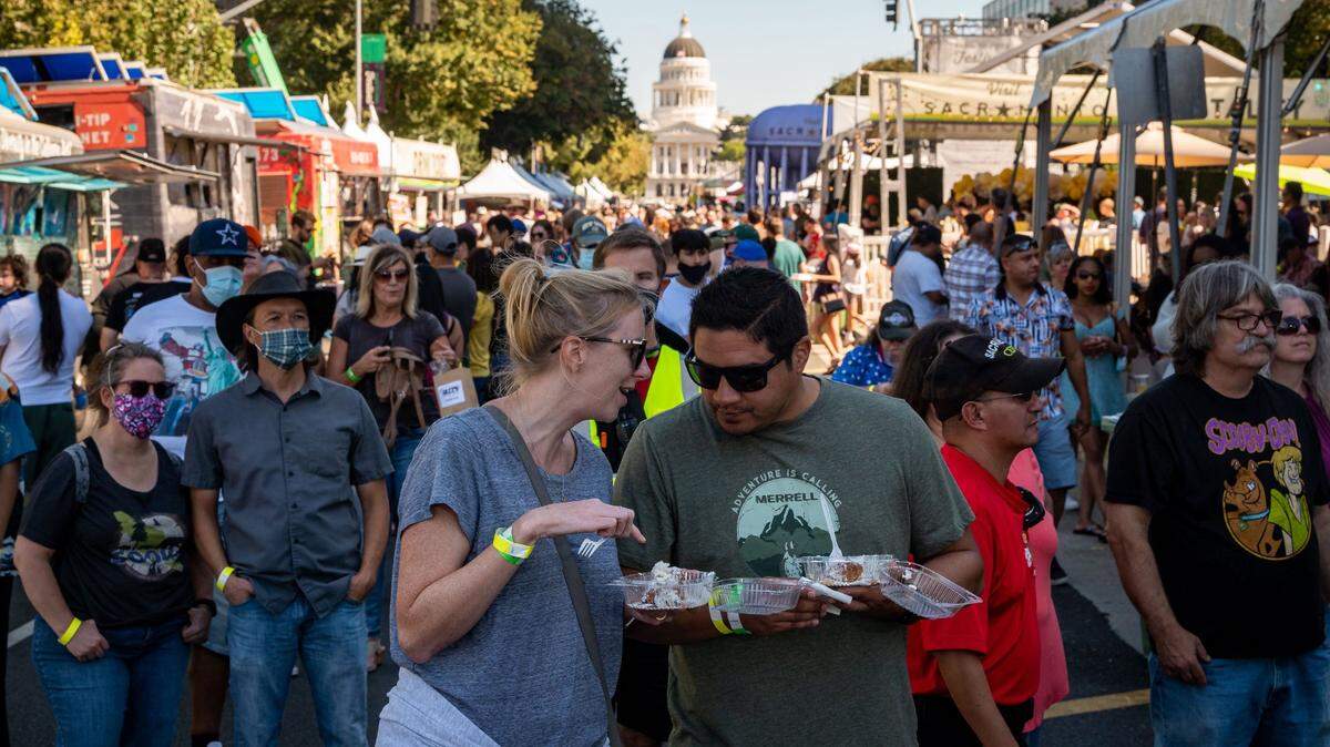 Emily Gardner, left, and Orlando Olivas, Sacramento resident, eat beignets and listen to live music at the Farm-to-Fork Festival in 2021, in downtown Sacramento. Olivas, who grew up in Sacramento and moved away 15 years ago, returned last January. “I’m surprised Sacramento has something like this going on,” he said. “Just to have the festival someplace downtown like this … it’s a good look for Sacramento.”