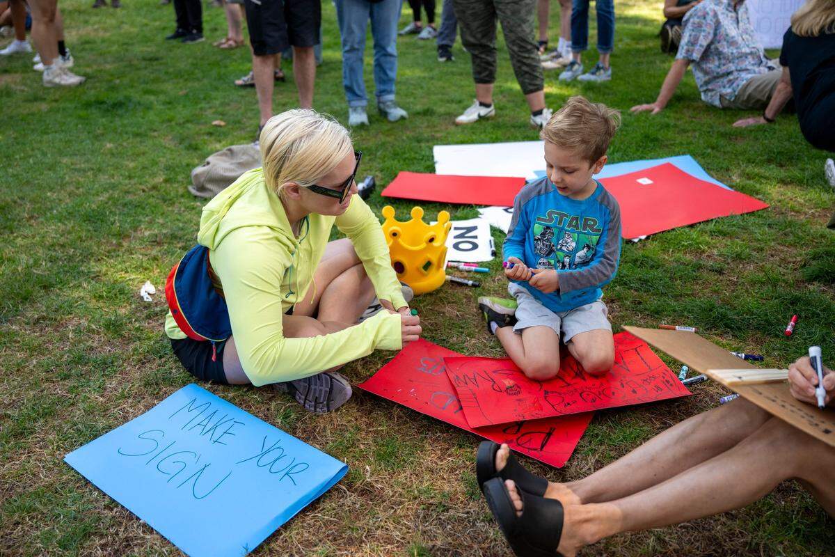 Sarah Turgasen, left, and Freddy Baiocchi, 5, draw a sign on state Capitol lawn during the “No Kings” protest against the Trump administration in downtown Sacramento on Saturday.