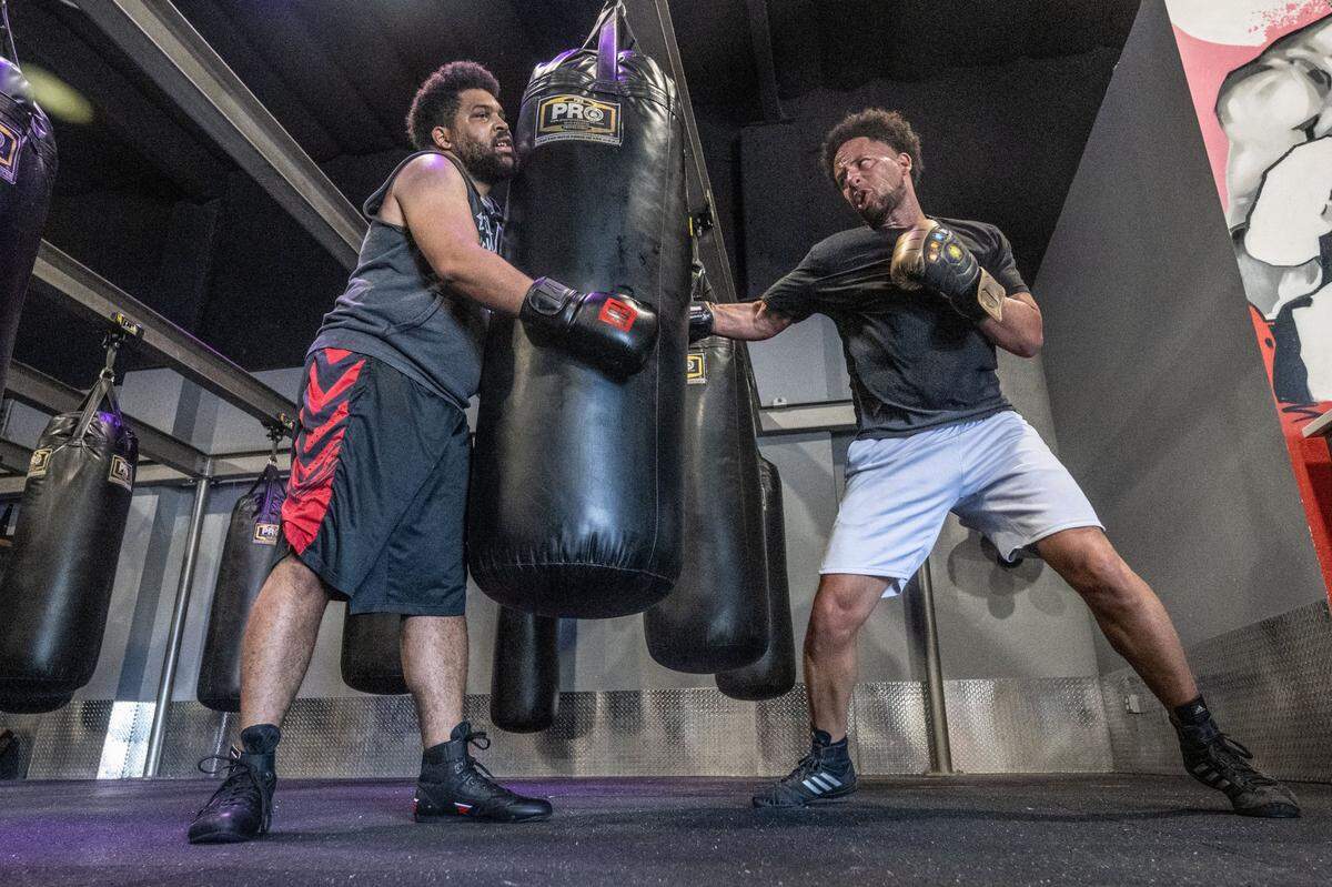 Sacramento Bee opinion columnist LeBron Hill, left, holds a punching bag during a boxing workout with Sacramento State President Luke Wood last month at Flawless Boxing & Fitness in Sacramento.