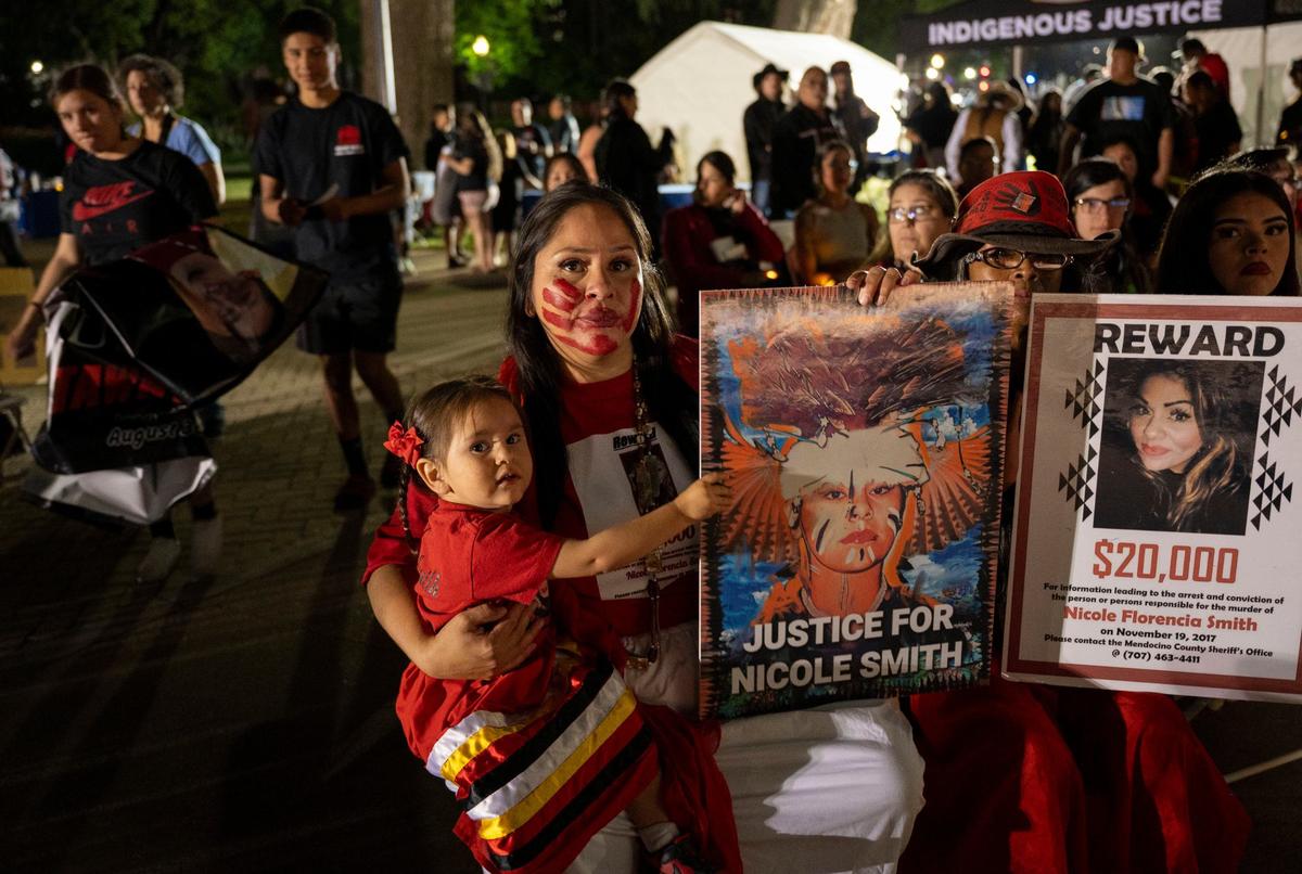 Bernadette Smith sits with a red handprint painted across her face with her daughter Chishkaleh Flores, 2, at the Missing and Murdered Indigenous People vigil at the Capitol on Wednesday, May 1, 2024. She holds a sign of her sister, Nicole Smith, who was murdered in 2017 on the Manchester Rancheria. Her murder is now a cold case.