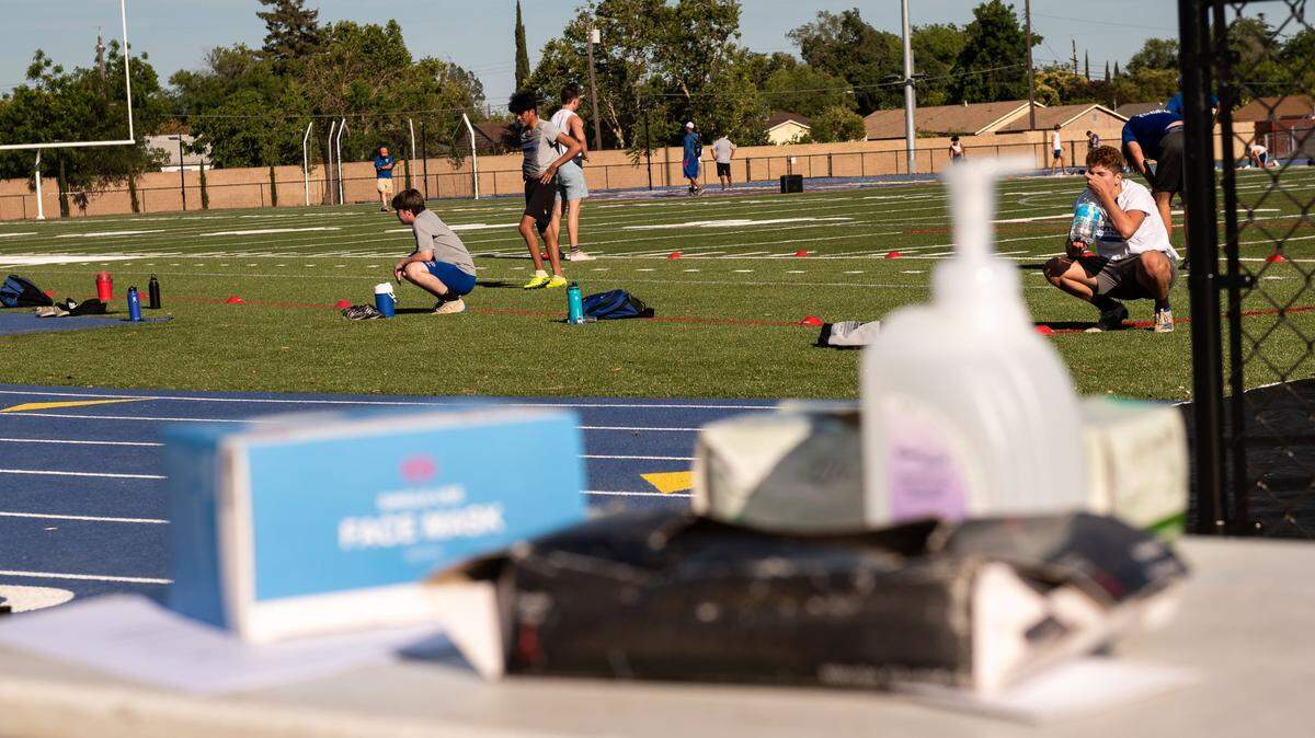 Christian Brothers High School football players break for hydration and recovery as seen past a check-in table set up with hand sanitizer, gloves, masks and more during their planned socially-distanced summer conditioning drills Thursday, June 18, 2020, at the Sacramento school.