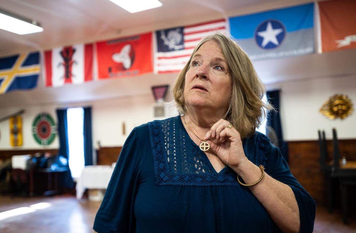 Sheila McNallen – wife of Stephen McNallen, founder of the whites-only religious organization Asatru Folk Assembly – talks about the sun cross around her neck while “kindred flags” hang behind her in the church’s “Odinshof” on July 27, 2021, in Brownsville in Yuba County.