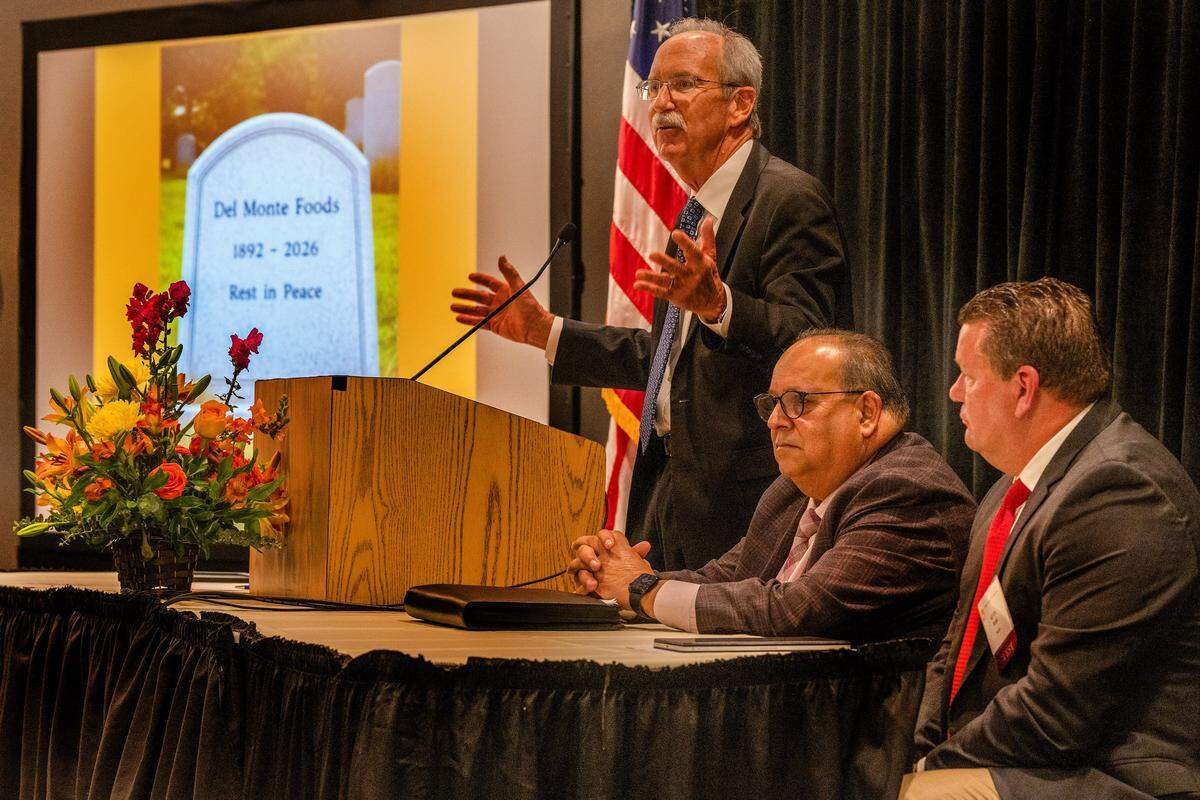 Rich Hudgins, president of the California Canning Peach Association, speaks about the demise of Del Monte Foods while displaying a picture of a tombstone alongside Ranjit Davit, center, the association’s chairman and a Sutter County peach grower, and Kevin Ralph, right, California state president of AgWest Farm Credit, at the association’s annual meeting on Feb. 4.