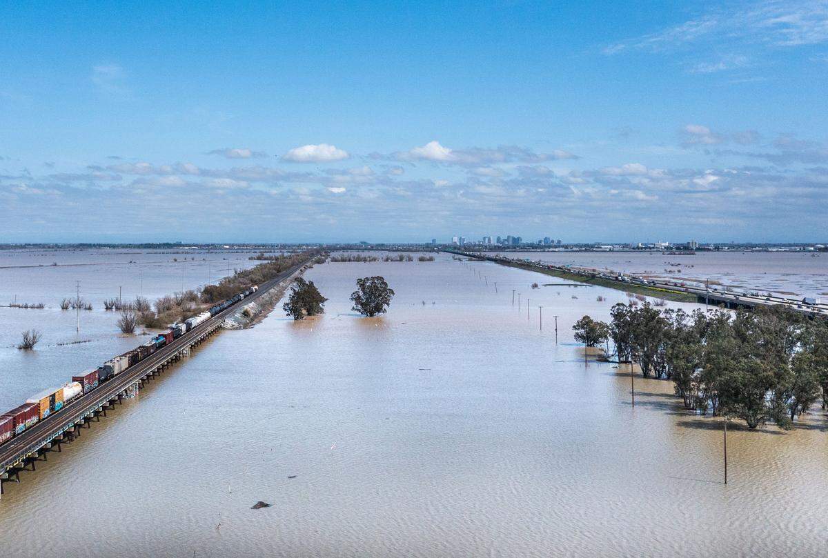 The Sacramento skyline floats over the flooded Yolo Bypass on Monday afternoon. The bypass, which is crossed by Union Pacific railroad tracks, left, and the roughly 3-mile Yolo Causeway that carries Interstate 80, right, floods when the surface of the Sacramento River reaches 32 feet and water overtops the Fremont Weir at its north end. It has been inundated twice this year after a dry spell going back to March 2019.