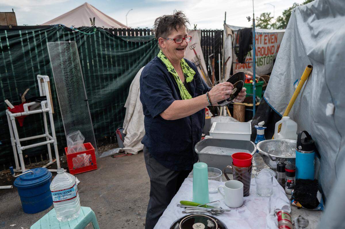 Joyce Williams washes dishes daily by heating plastic water containers in a pot on her propane gas stove at Camp Resolution last week. There is no water or electricity inside the city-provided trailers. The camp inhabitants use generators for fans to keep them cool and for lighting when the sun goes down.