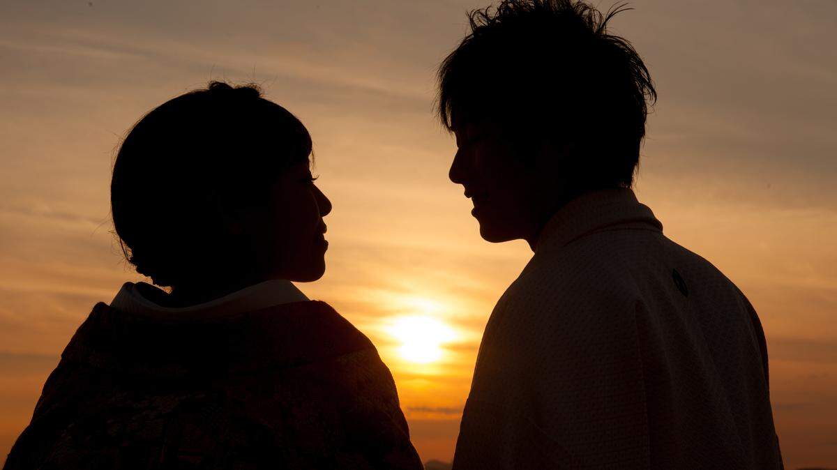 A silhouette of a couple with the setting sun between them.