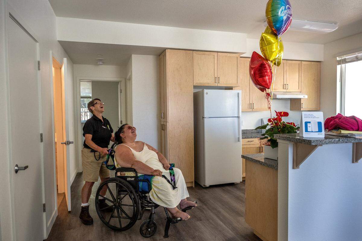 Holly Porter, a quadriplegic who was living in a hospital bed at Camp Resolution homeless encampment, is wheeled around her new apartment by Hope Cooperative’s Tracey Knickerbocker on Thursday. Knickerbocker had bought Holly a plant, balloons and assorted deli meats in celebration of her getting her keys and getting housed. “Relieved that it finally happened,” said Porter who sought housing for a year and a half. “I’m very excited. but I just don’t think it’s actually sunk in yet.”