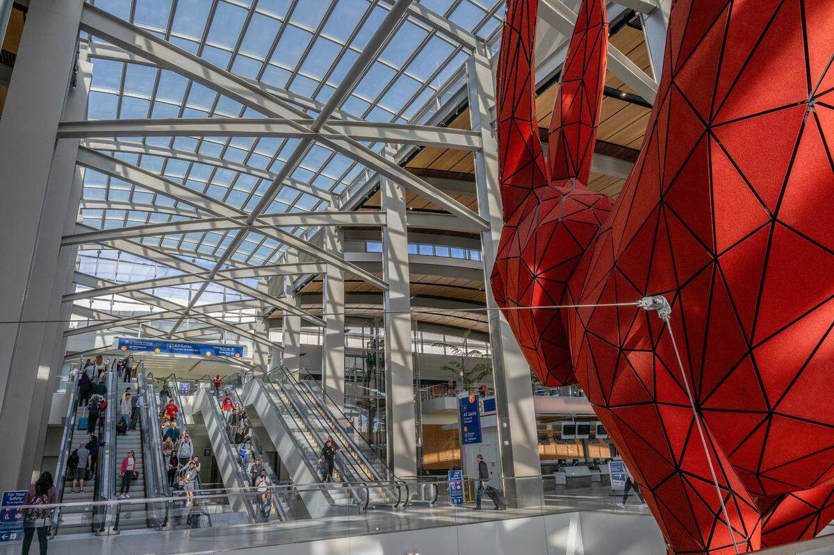 Travelers descend escalators under the watchful eye of “Leap,” the red rabbit sculpture by Lawrence Argent, as they make their way toward baggage claim in Sacramento International Airport’s Terminal B on Nov. 22, 2023, the day before Thanksgiving. 