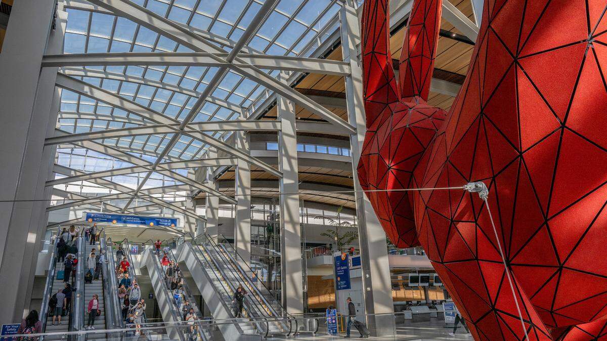 Travelers descend escalators under the watchful eye of “Leap,” the red rabbit sculpture by Lawrence Argent, as they make their way toward baggage claim in Sacramento International Airport’s Terminal B on Nov. 22, 2023, the day before Thanksgiving.