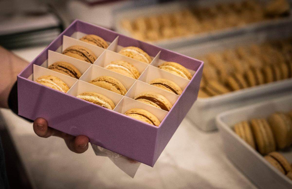 An employee at Ginger Elizabeth Patisserie holds a box of macarons on Tuesday. Owner Ginger Elizabeth Hahn has had to adjust to inflation, with the higher cost of ingredients such as butter. Her French-inspired bakery has only hiked the price of macarons or chocolates made at its sister shop by 25 cents each, but she expects the store’s profits to decline.