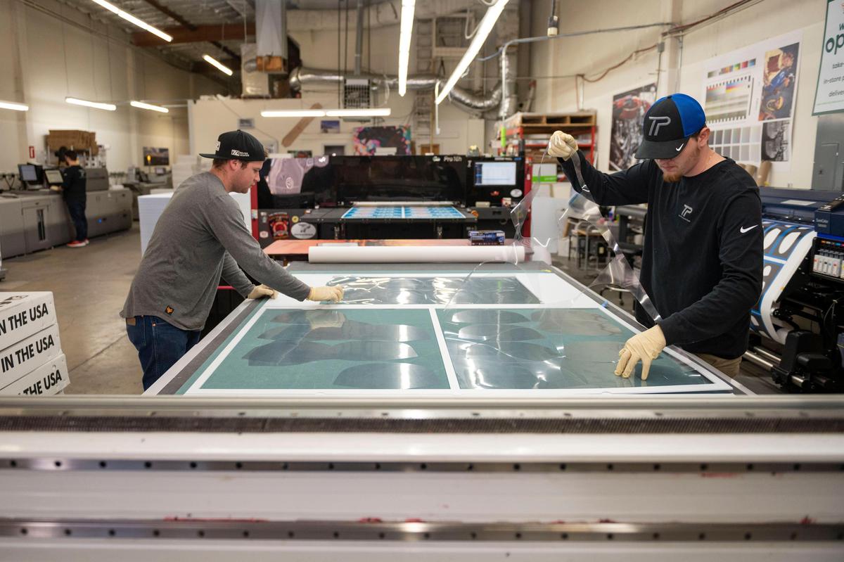 Hunter Poole and Douglas Neely collect recently cut plastic face masks at Time Printing that can be used as personal protective equipment for a variety of businesses to help fight the spread of coronavirus Friday, April 3, 2020. Business has slowed for the family run print shop since a stay-at-home order was issued in California, so the company started producing face masks as a way to keep the shop running and to help fill the nationwide shortage of protective equipment during the COVID-19 pandemic.