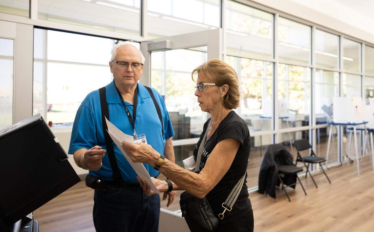 Voter Rebecca Wilson is instructed by Ray Falk before inserting her ballot into the voting machine at the Placer County Clerk-Recorder-Elections Office in Rocklin on Tuesday, Oct. 28, 2025.