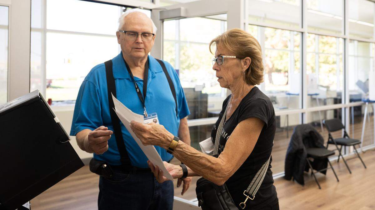 Voter Rebecca Wilson is instructed by Ray Falk before inserting her ballot into the voting machine at the Placer County Clerk-Recorder-Elections Office in Rocklin on Tuesday, Oct. 28, 2025.