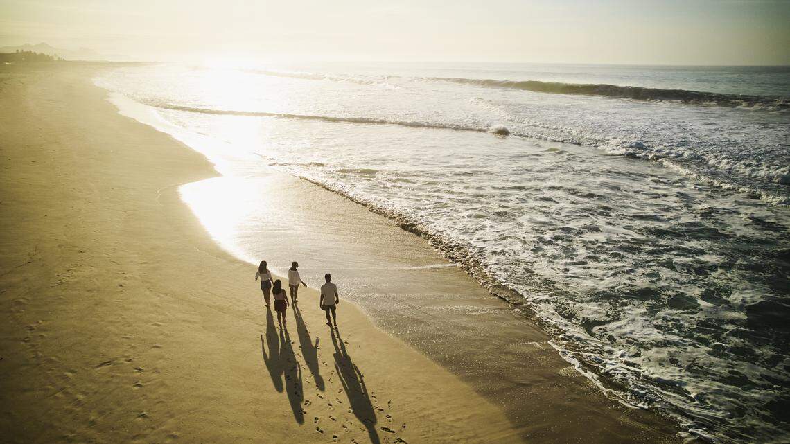 Wide aerial shot of family walking on beach at sunrise while on vacation