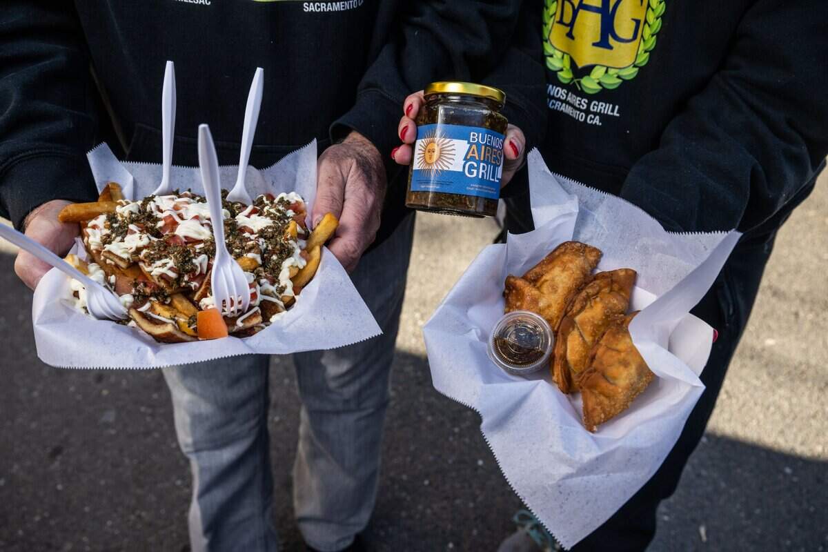 Ruben Bozzalla, left, and his daughter Estefania Bozzalla hold some of the food they serve from their Buenos Aires Grill earlier this month at the Midtown Farmers Market. Ruben is holding their best seller “messy” fries topped with chicken, mayonnaise and tomatoes and Estefania holds empanadas and a jar of chimichurri.